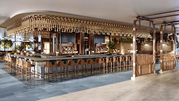 Un área de bar moderna con una barra curva, diversas opciones de asientos y un techo decorativo.