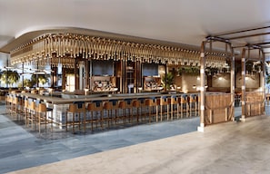 Un área de bar moderna con una barra curva, diversas opciones de asientos y un techo decorativo.