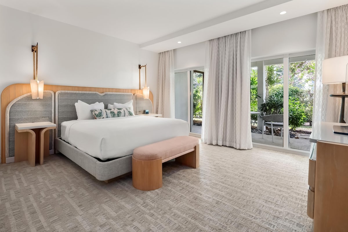 Habitación de hotel moderna con una cama grande, mesitas de noche, un banco y vistas al exterior.