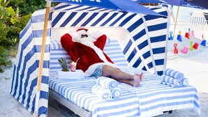 A beach cabana with striped bedding and a red blanket, a pineapple drink, and a beach umbrella. - Naples Grande Beach Resort (Naples)
