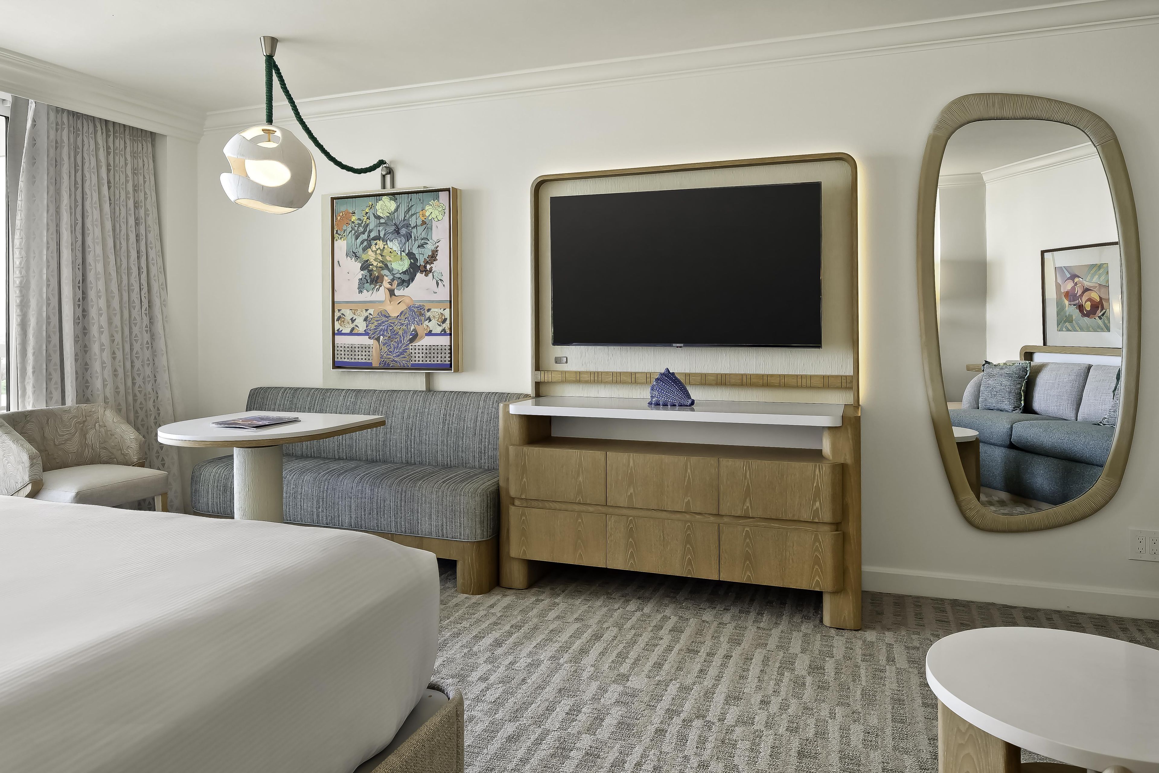A hotel room with a bed, a sofa, a small table, a TV, and a mirror.