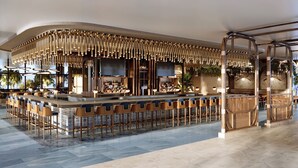 A bar area with a curved ceiling, bar stools, and a counter with bottles. - Naples Grande Beach Resort (Naples)