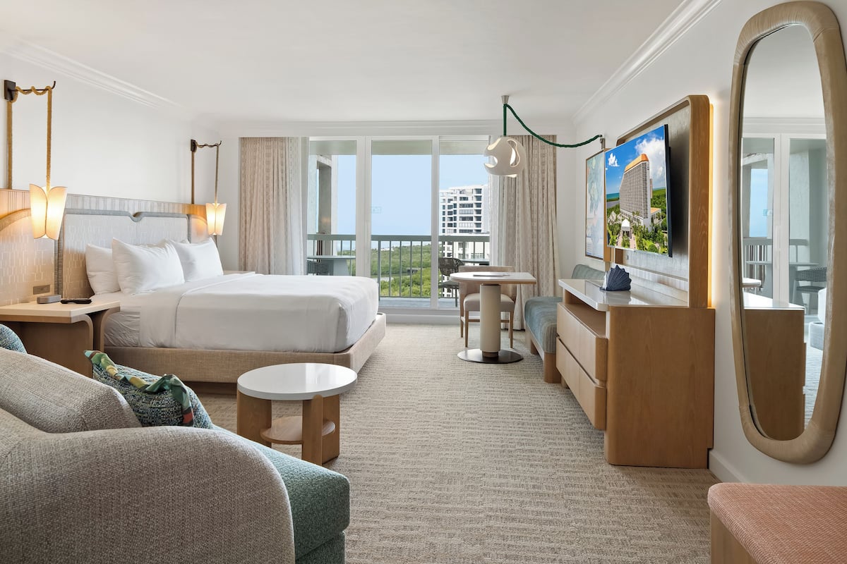 Habitación de hotel con cama, escritorio, silla, televisión y un amplio ventanal.