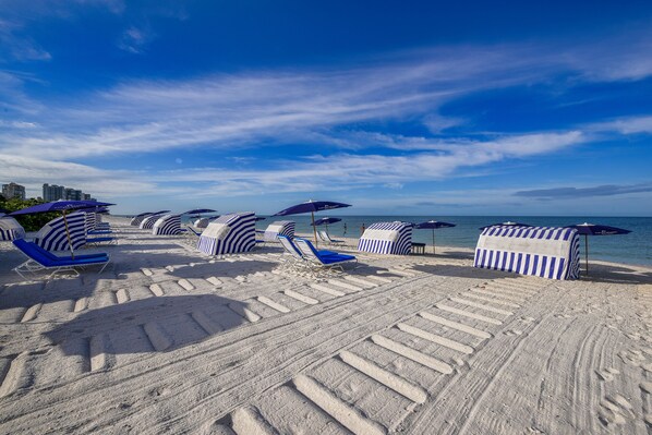 A beach with striped beach umbrellas and lounge chairs. - Signia Hilton Naples Grande Beach Resort (Naples)
