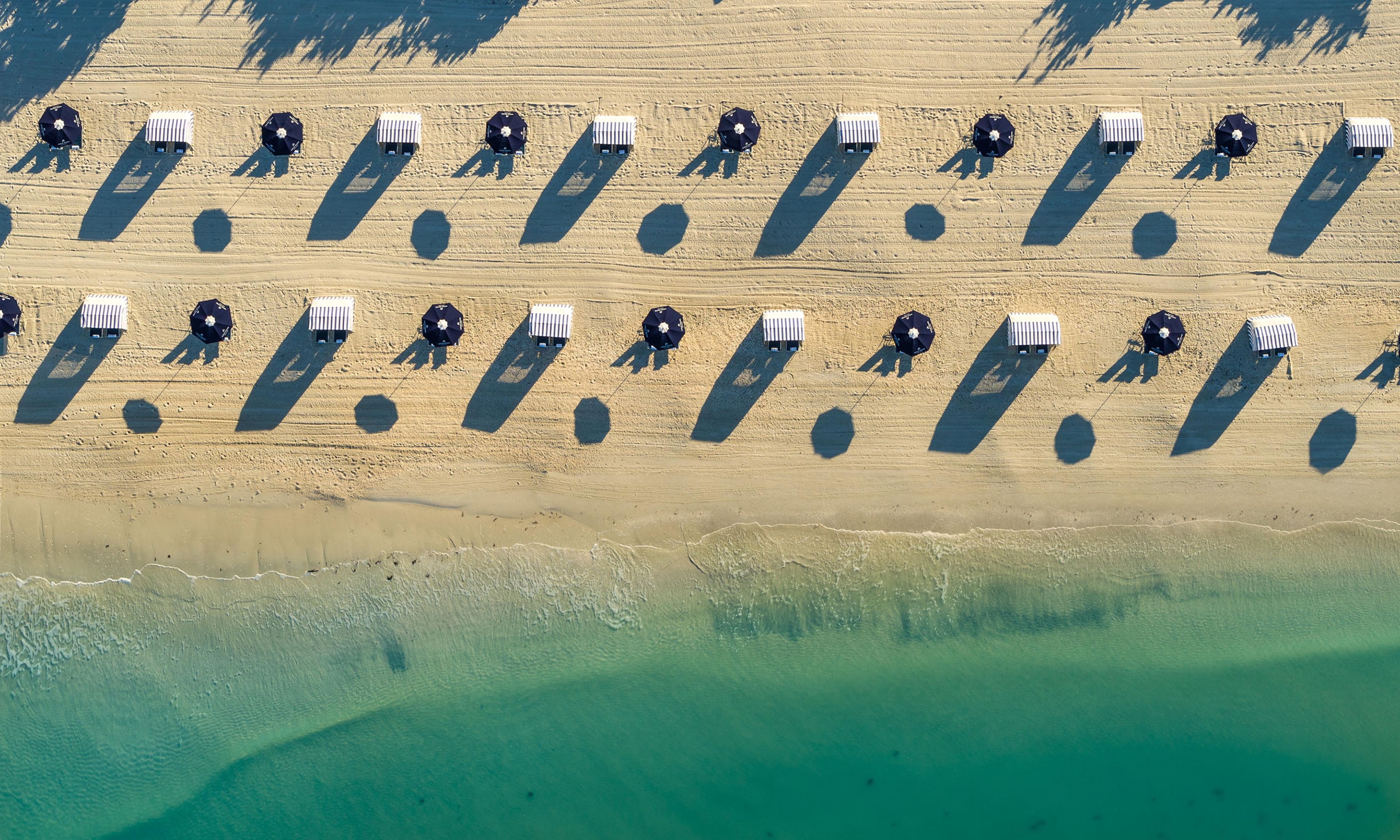 Vista aérea de una playa con hileras de sombrillas y cabañas de playa.