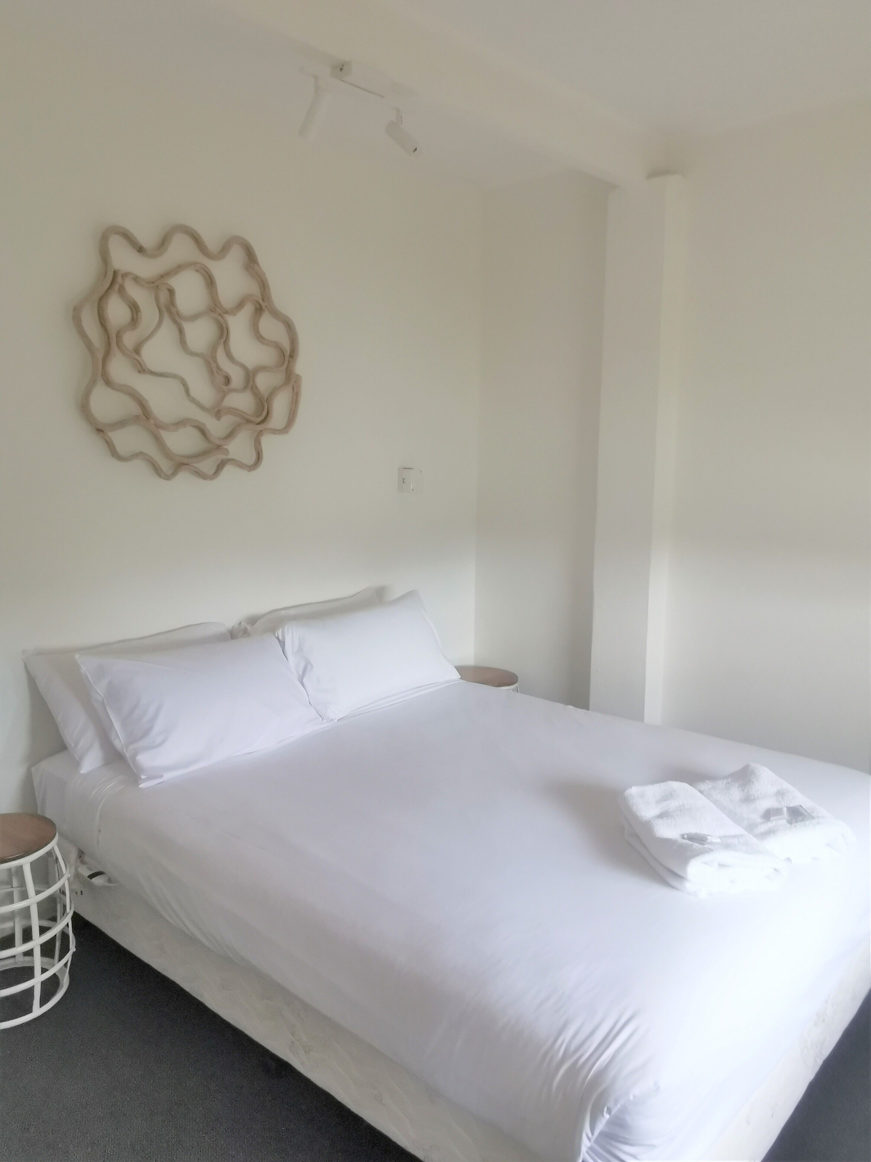 A minimalist bedroom with a large bed, white bedding, a decorative wall piece, and a small bedside table.