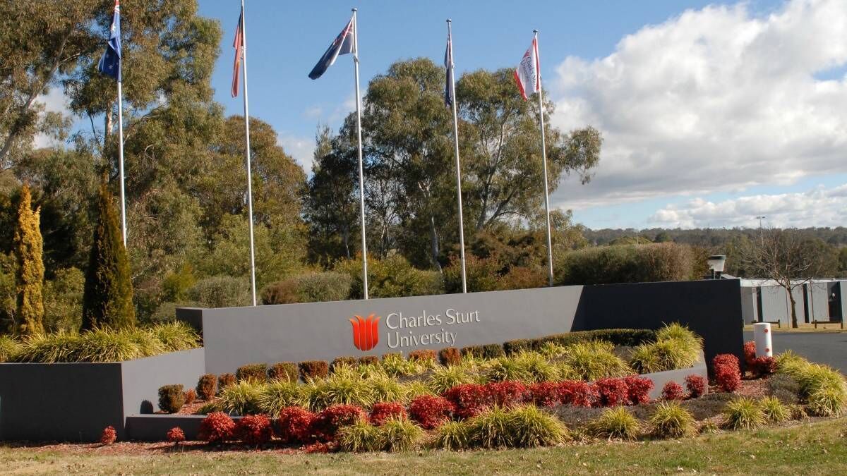 Señal de la Universidad Charles Sturt con varias banderas y jardines ajardinados.
