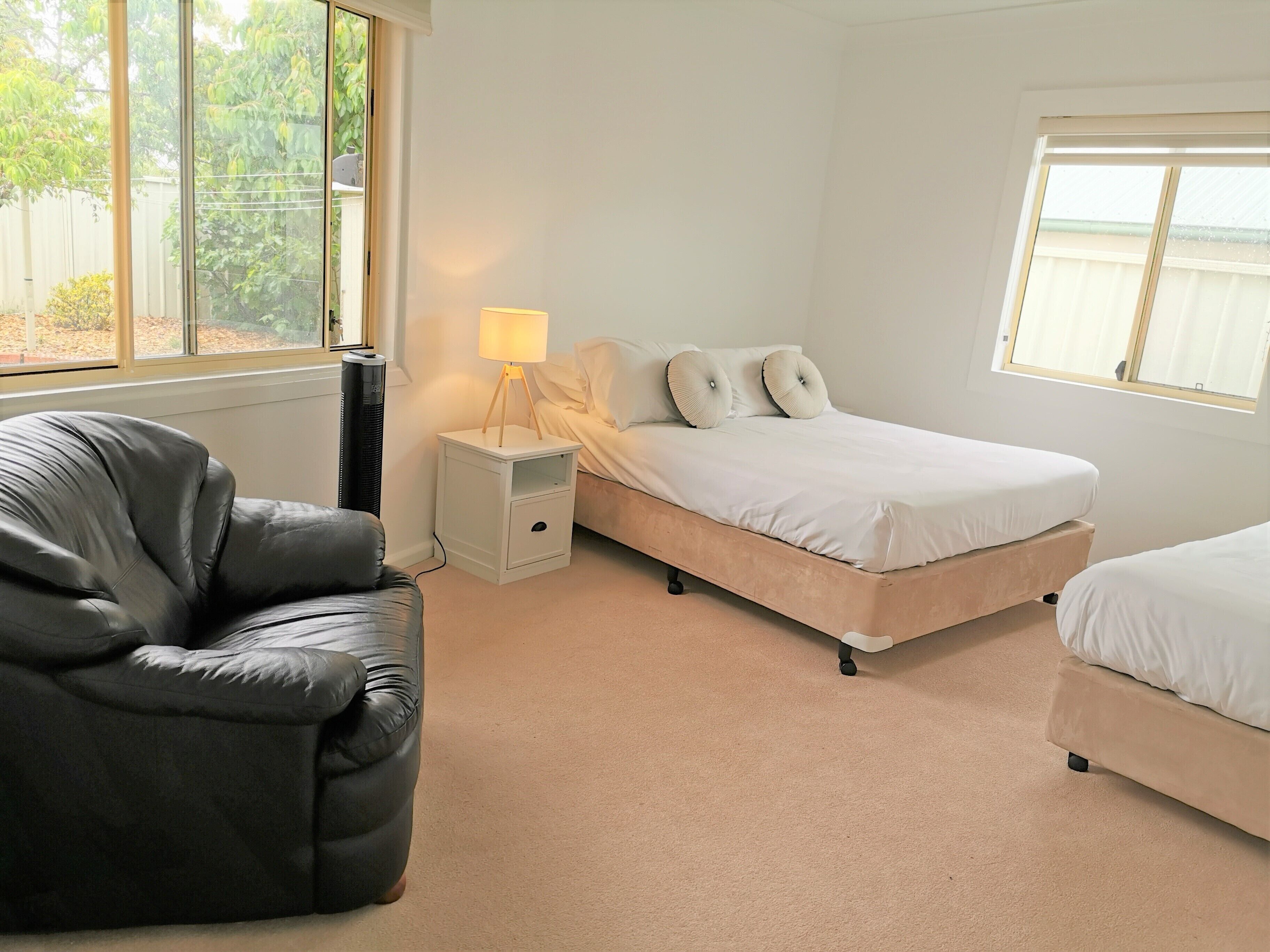 A bedroom with a bed, a chair, a bedside table with a lamp, and a window.