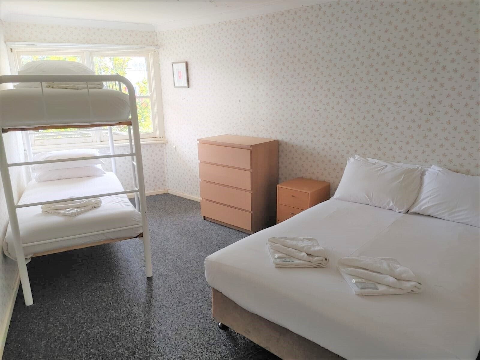 A hotel room with a bunk bed, a single bed, a dresser, and a small cabinet.