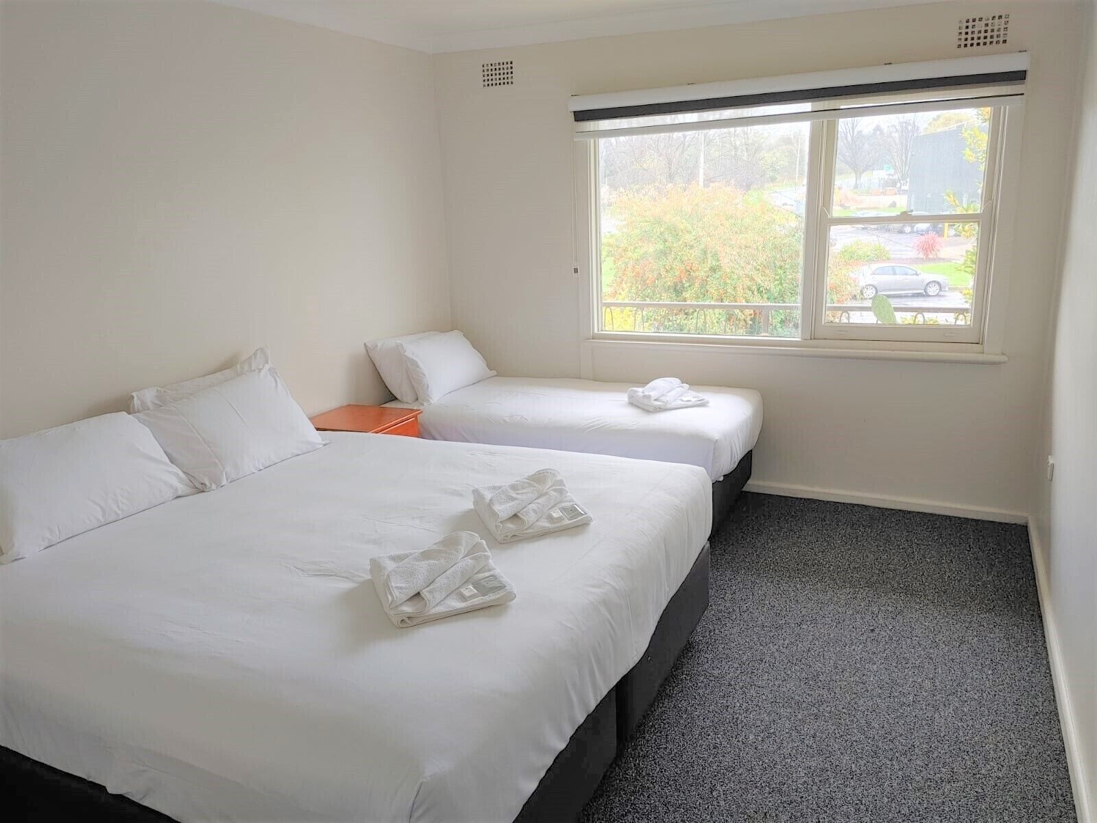 Een hotelkamer met twee bedden, een raam met uitzicht op bomen en een parkeerplaats, en een vloerbedekking.