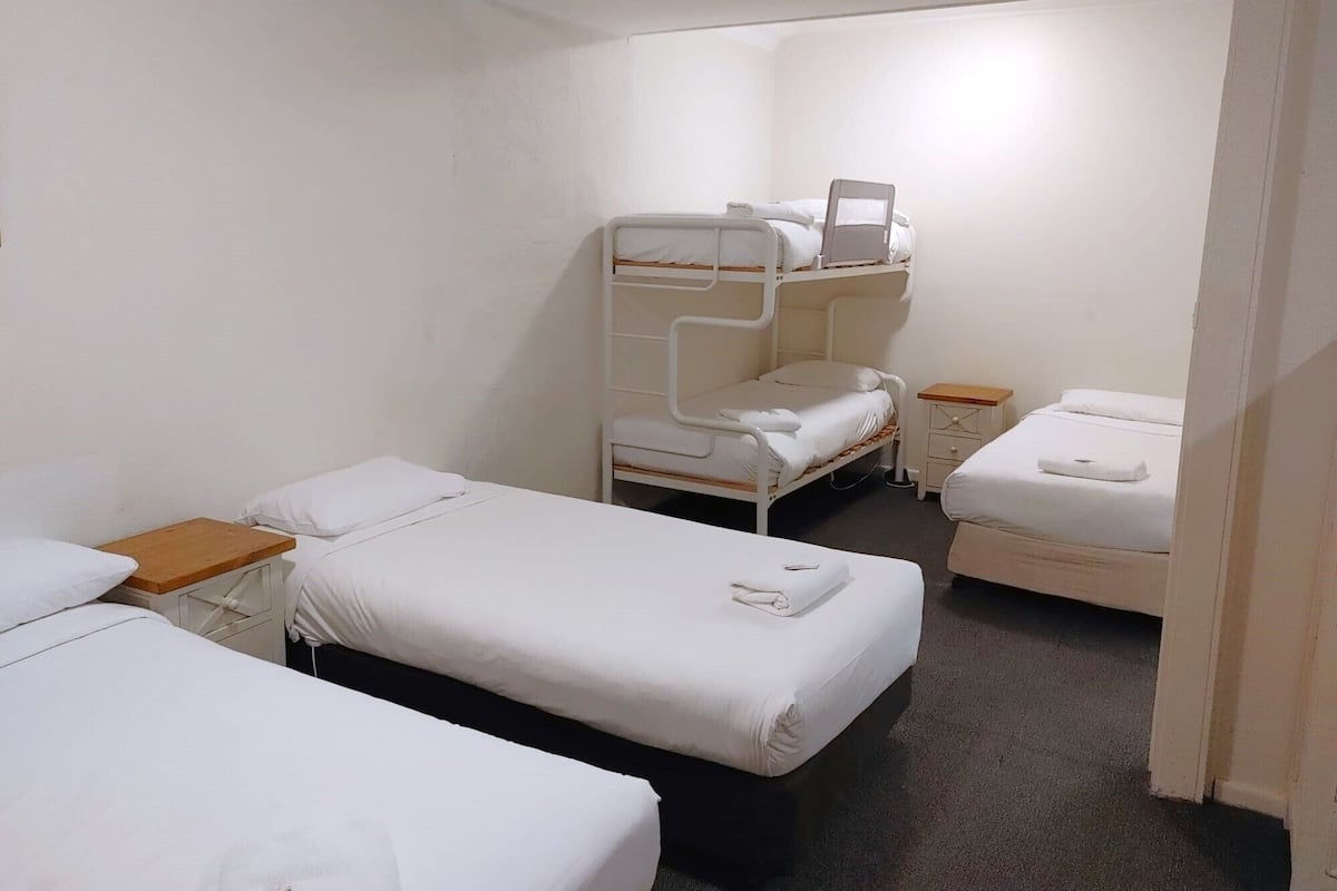 A room with three bunk beds, each with a wooden nightstand and a white pillow.