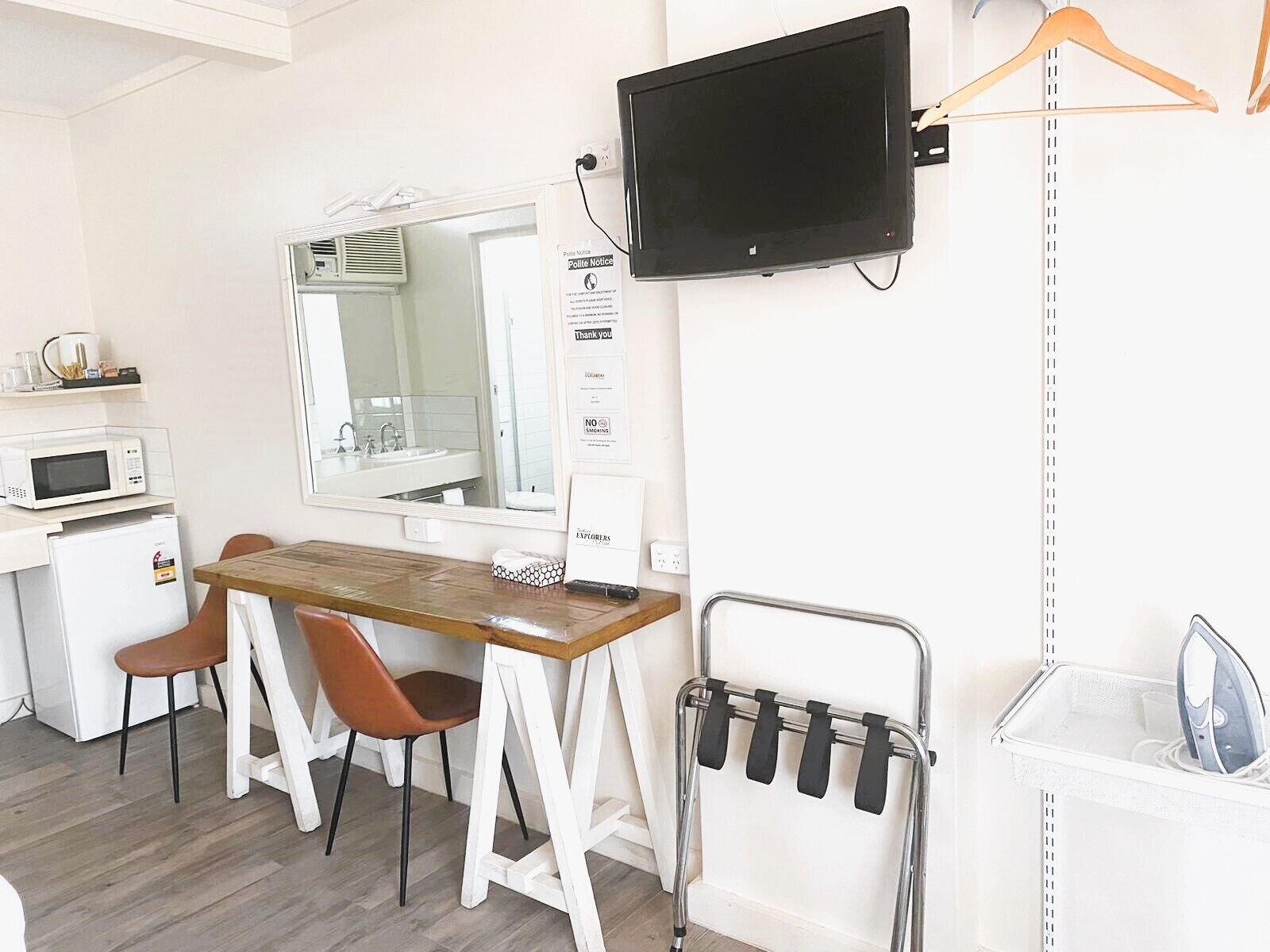 A small kitchenette with a microwave, a sink, and a mirror. There is a wooden table with two chairs and a metal rack with hangers.