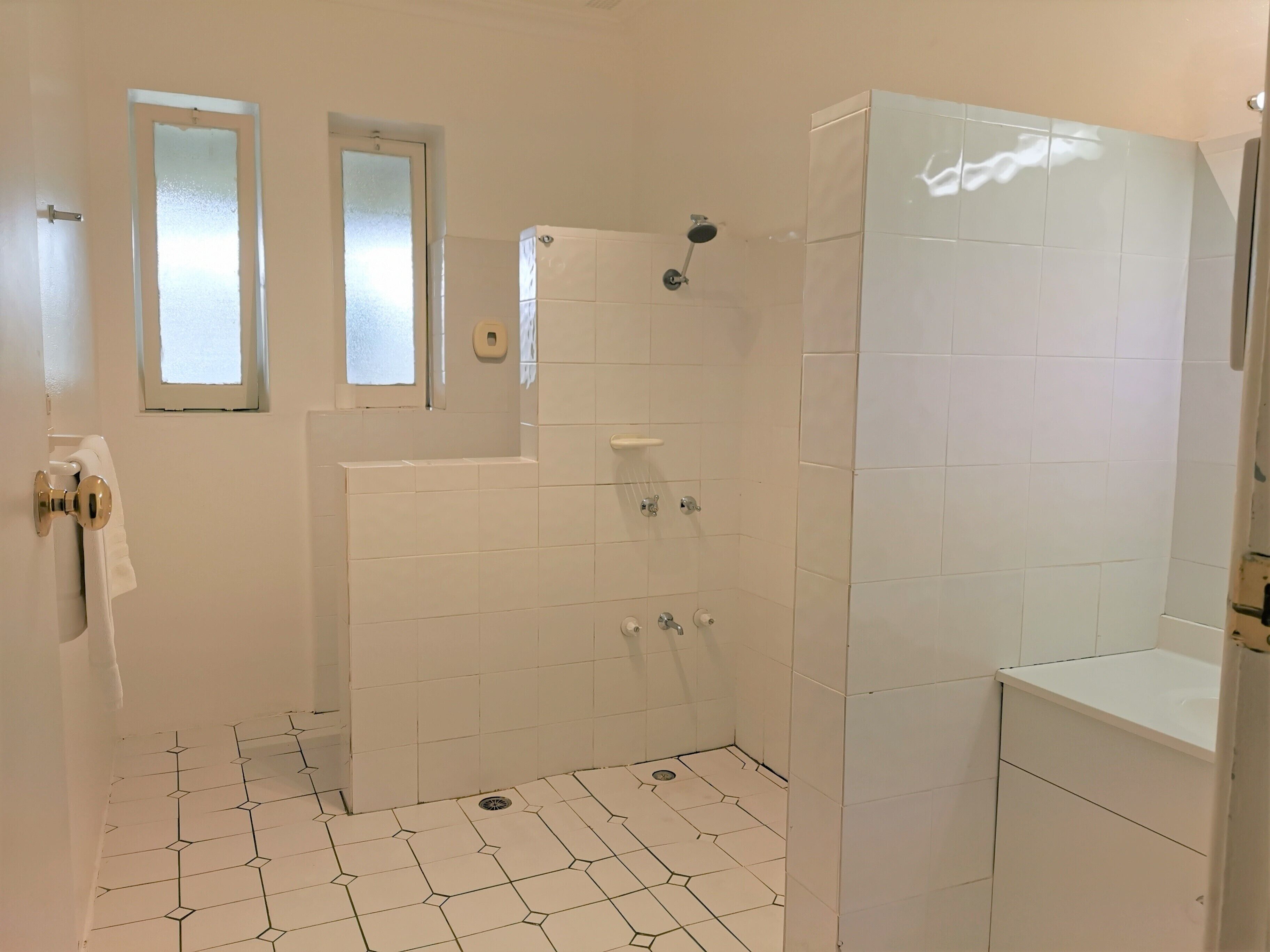 A bathroom with white tiled walls and floor, a shower area, a toilet, and a sink.