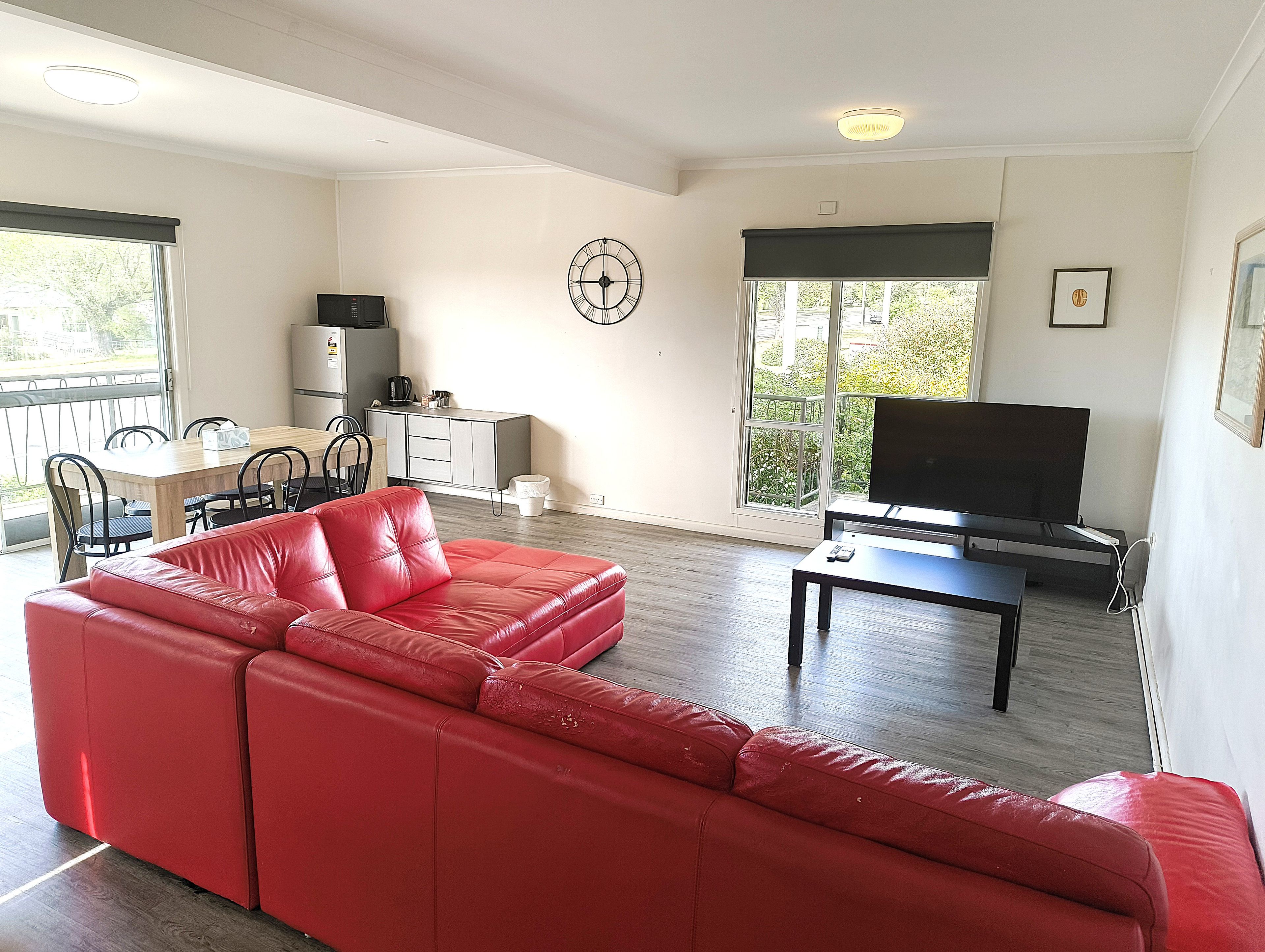 Una sala de estar con sofá rojo, televisor, mesa de comedor con sillas, zona de cocina y balcón con vistas.