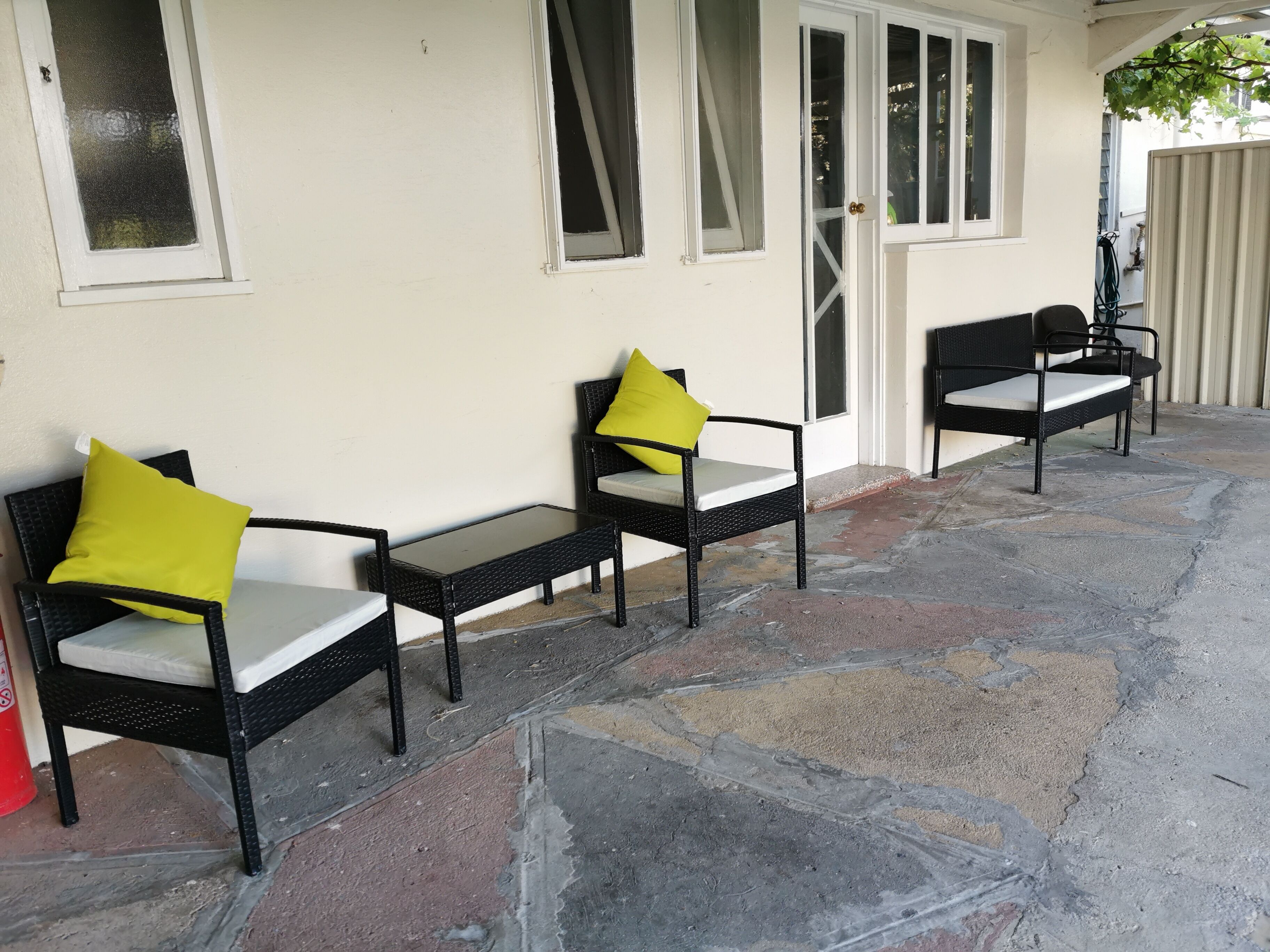 Une terrasse avec deux chaises en osier noir et une petite table, chacune agrémentée d’un coussin jaune.