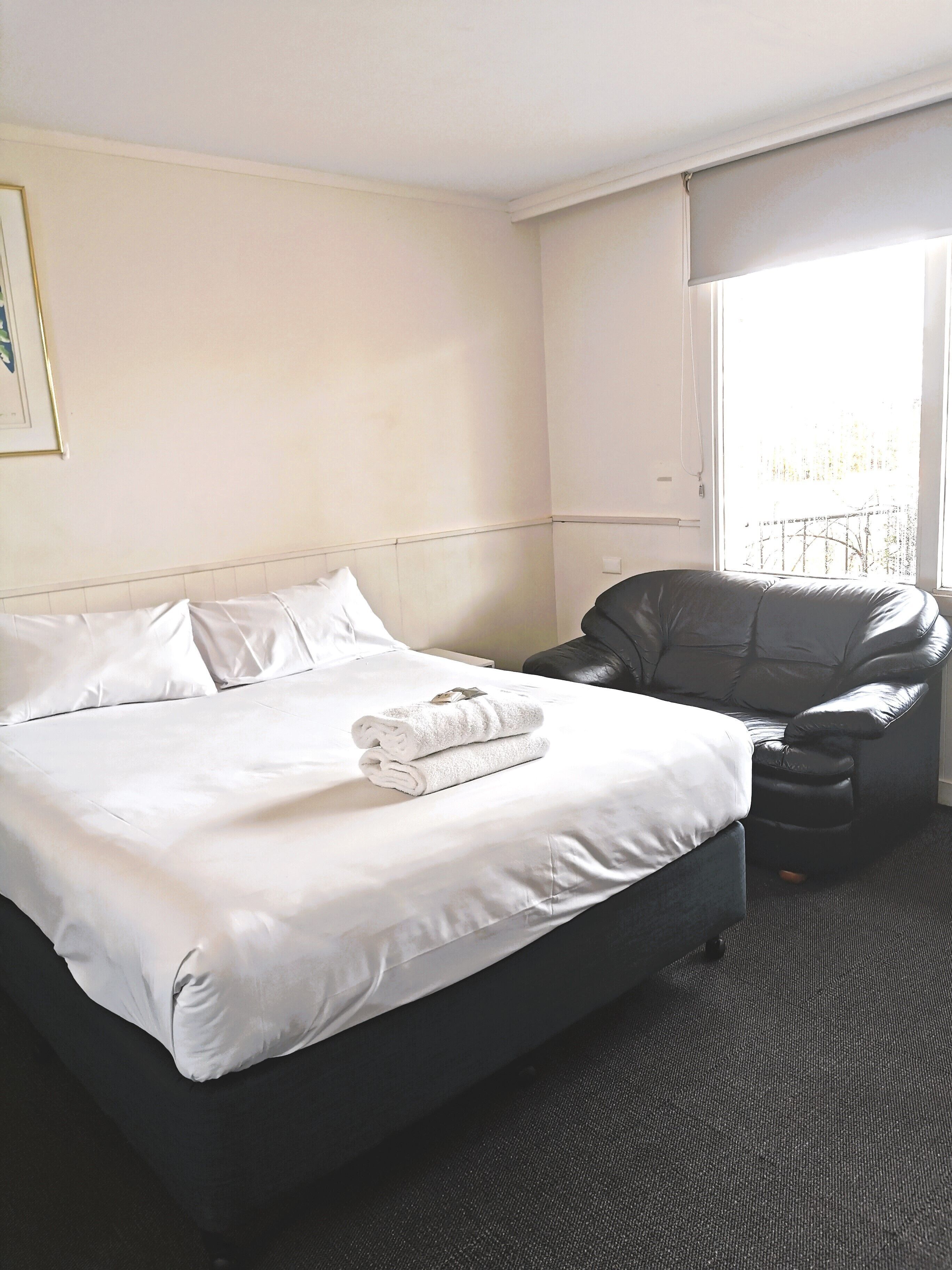 A hotel room with a bed, a black leather chair, and a window with a view.