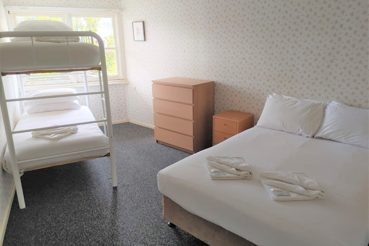 Ein Hotelzimmer mit Etagenbett, einem Einzelbett, einem Schminktisch und einem kleinen Schrank.