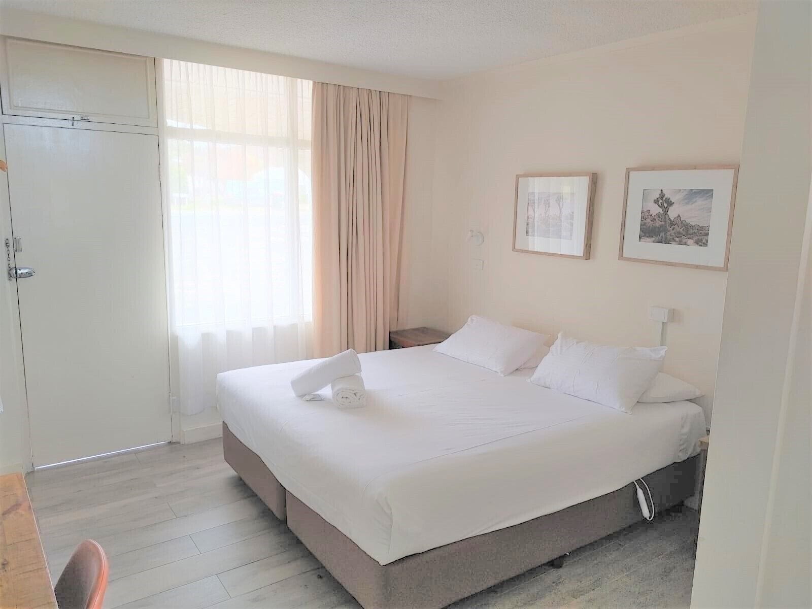 Habitación de hotel con una cama grande, una mesita de noche, una silla y una ventana con cortinas.