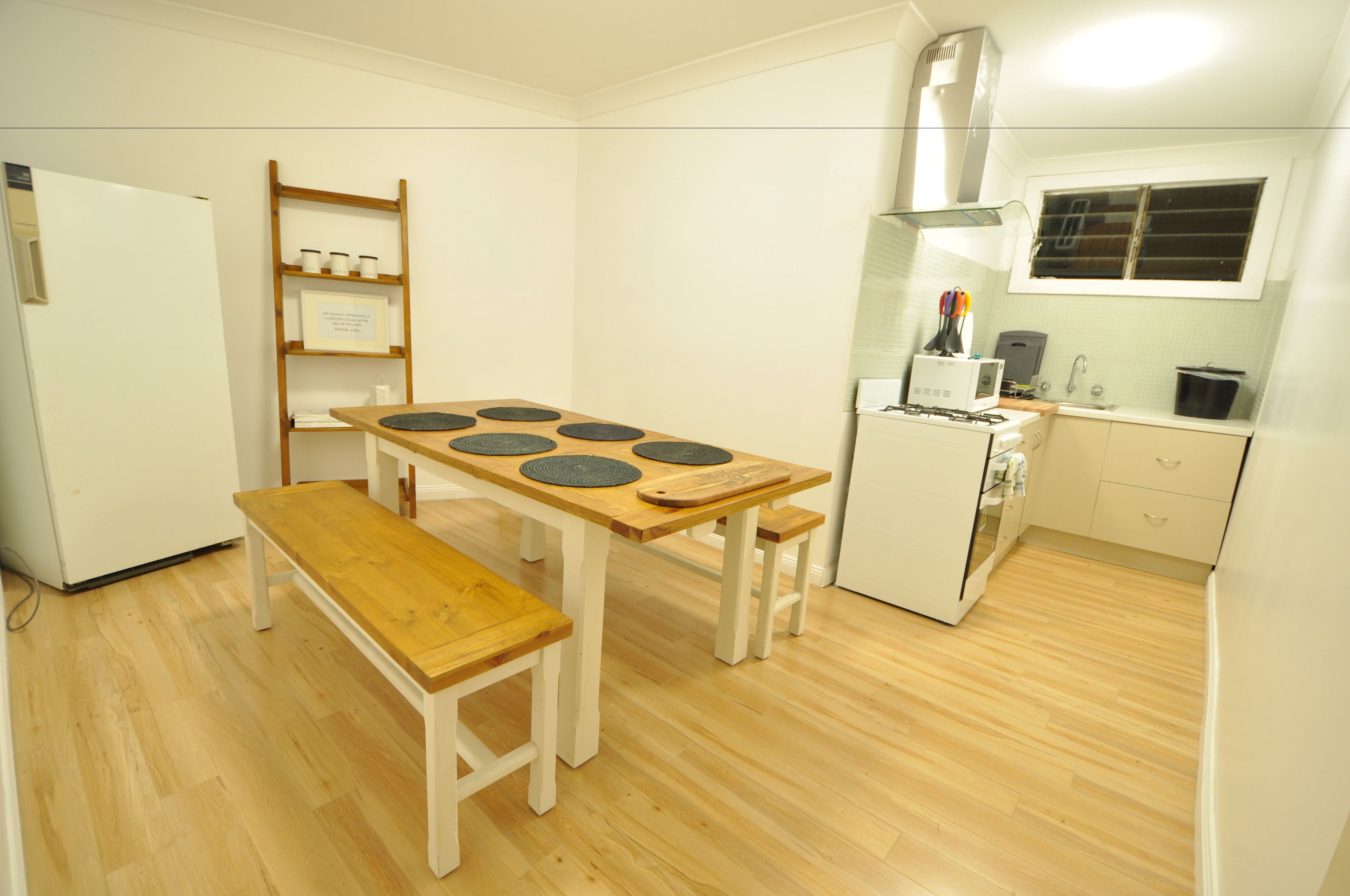 A compact kitchen with a wooden table, a bench, a refrigerator, a stove, and a window.