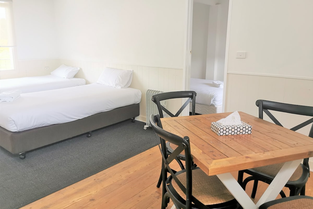 A room with two beds, a wooden table with chairs, and a radiator.