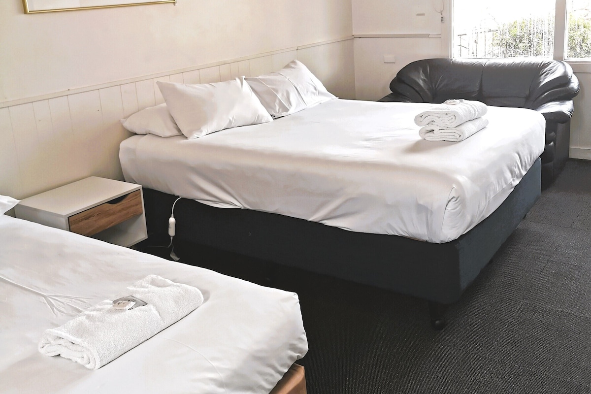A hotel room with two beds, a small bedside table, a chair, and a large window.