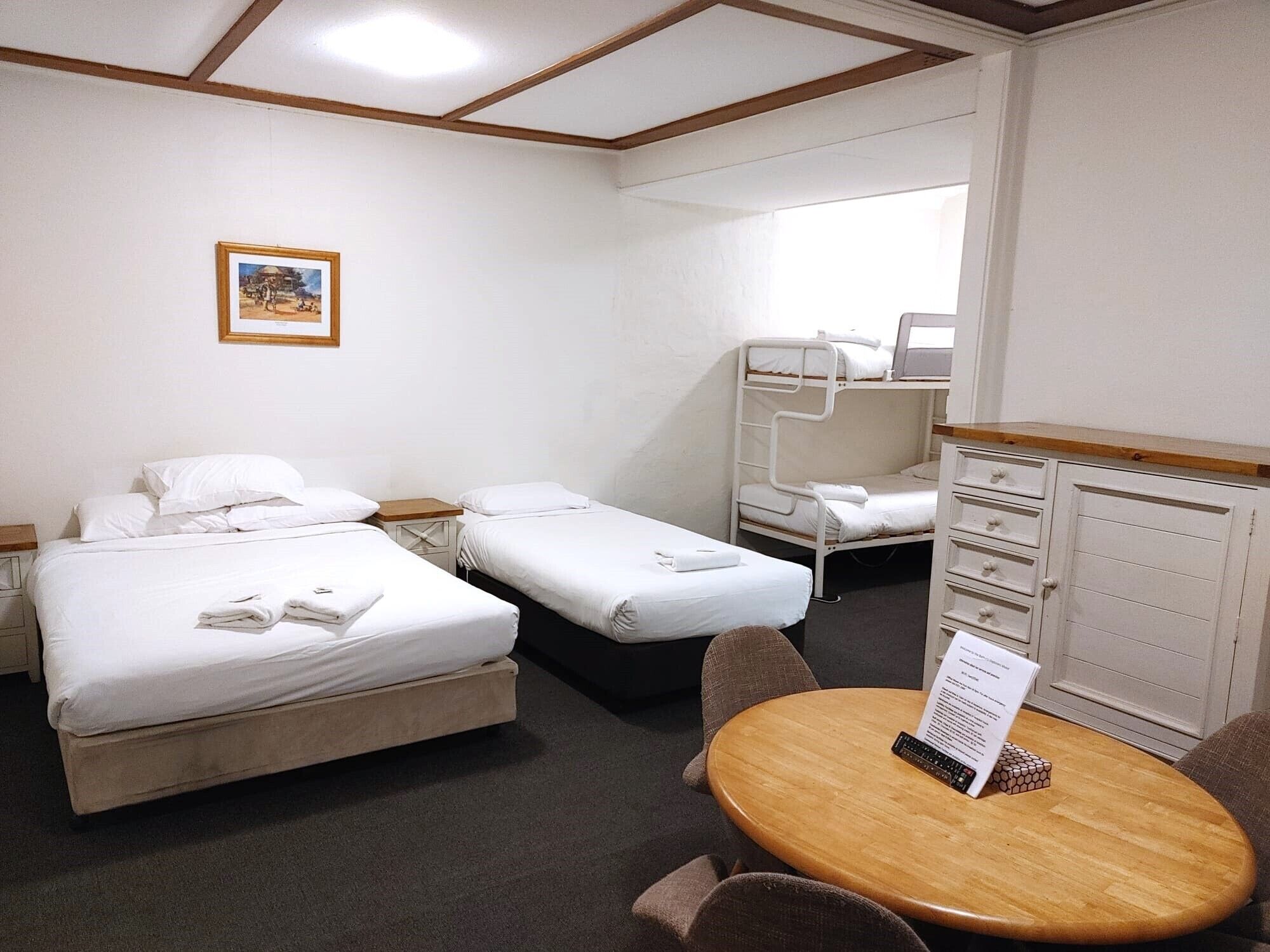 Une chambre d’hôtel avec deux lits simples, un lit superposé, une table en bois avec un menu et un petit placard.