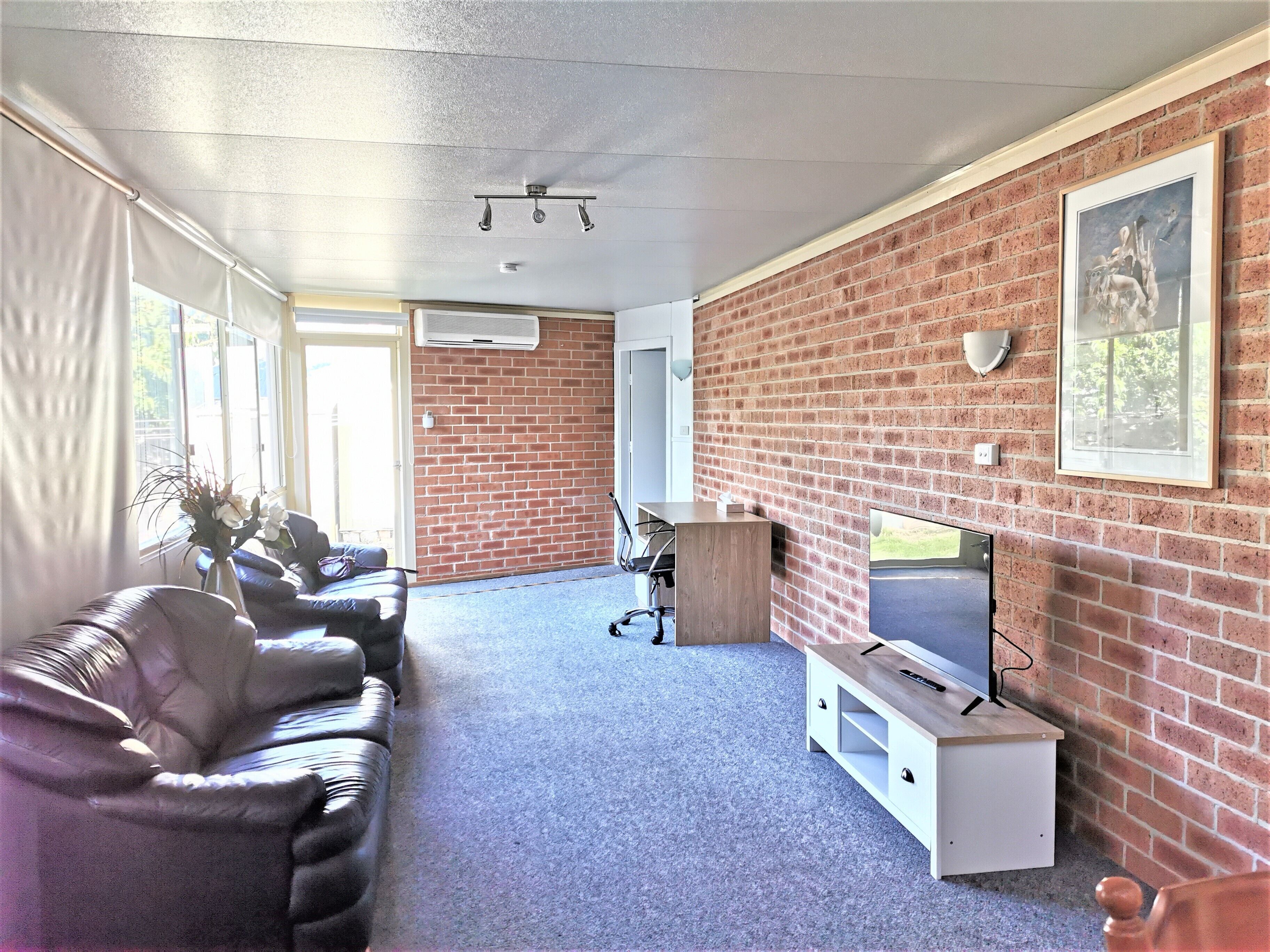 Een moderne woonkamer met een bakstenen muur, een flatscreen televisie, leren banken en een klein houten tafeltje.