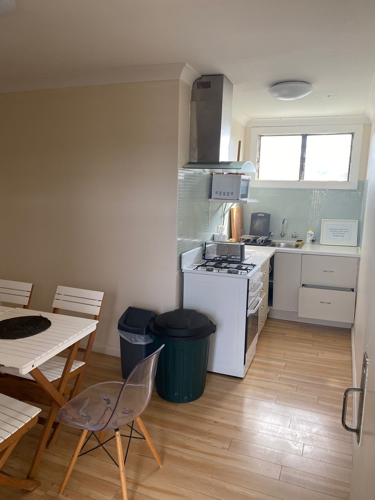 Cocina compacta con estufa, microondas y pileta. Hay una mesa de comedor con sillas y un basurero.