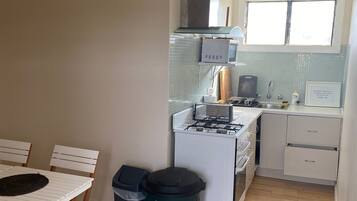 Cocina compacta con estufa, microondas y pileta. Hay una mesa de comedor con sillas y un basurero.
