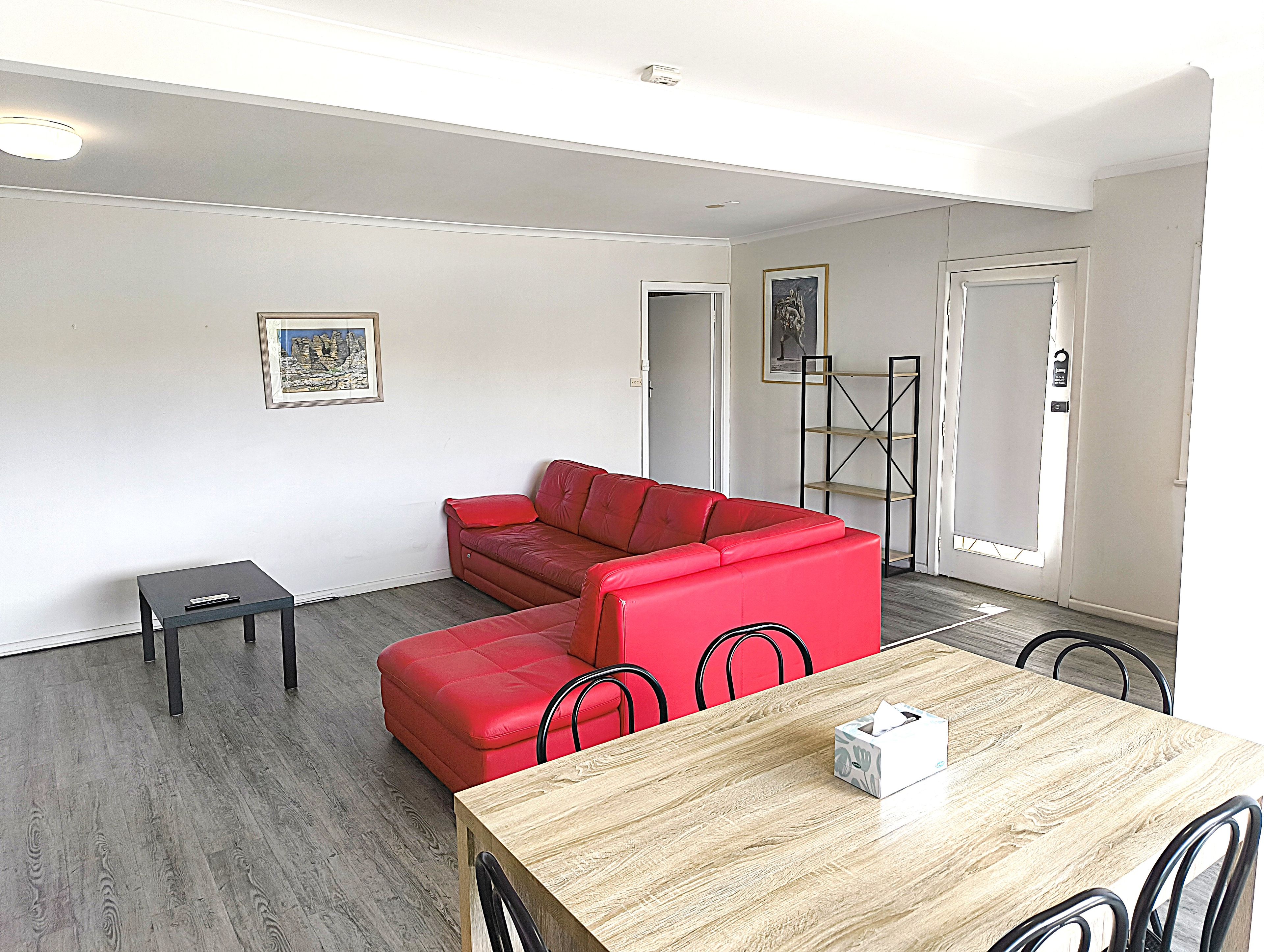 A living room with a red sectional sofa, a small table, and a dining table with chairs.