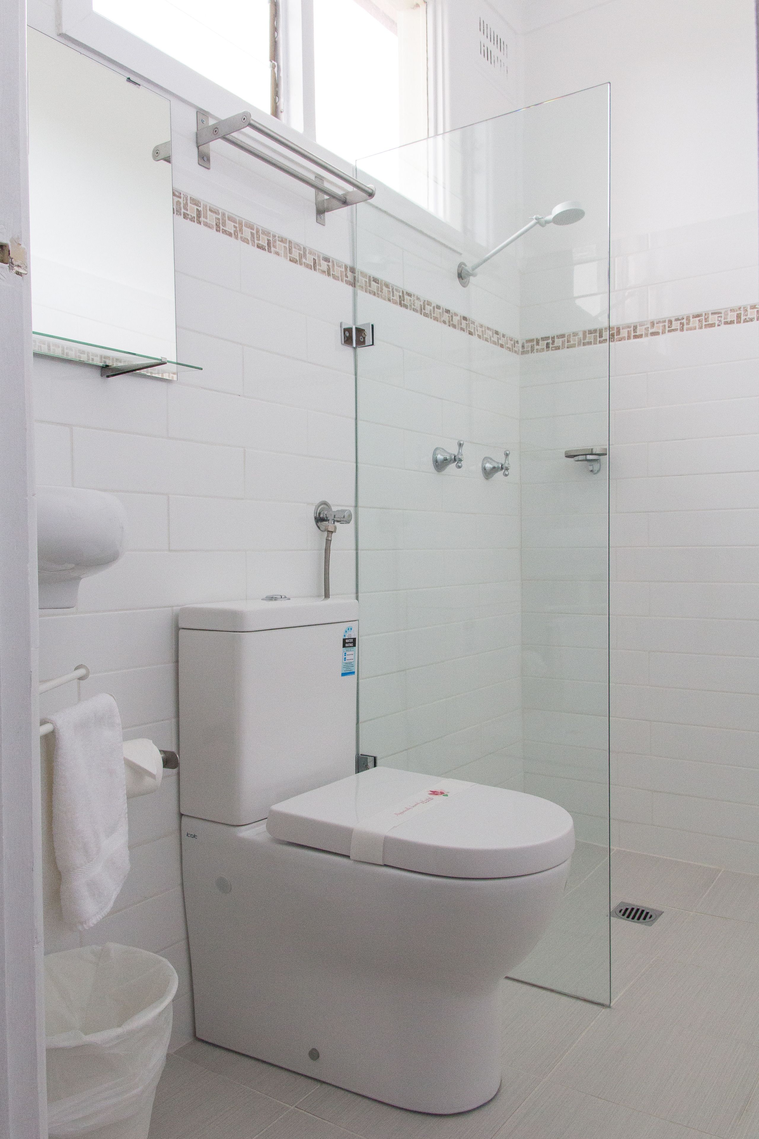 Un baño moderno con cabina de ducha de vidrio, inodoro blanco y estante de vidrio sobre el lavabo.