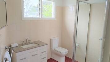Ein Badezimmer mit Fenster, Waschbecken, Toilette und Dusche.