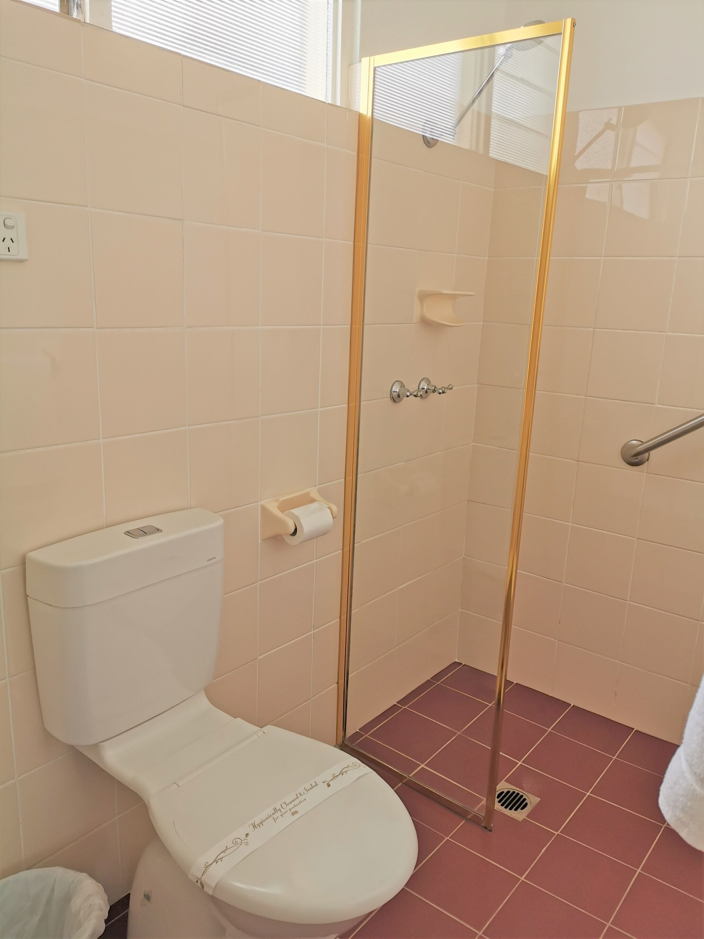 Un baño con inodoro, ducha con puerta de vidrio y suelo de baldosas.