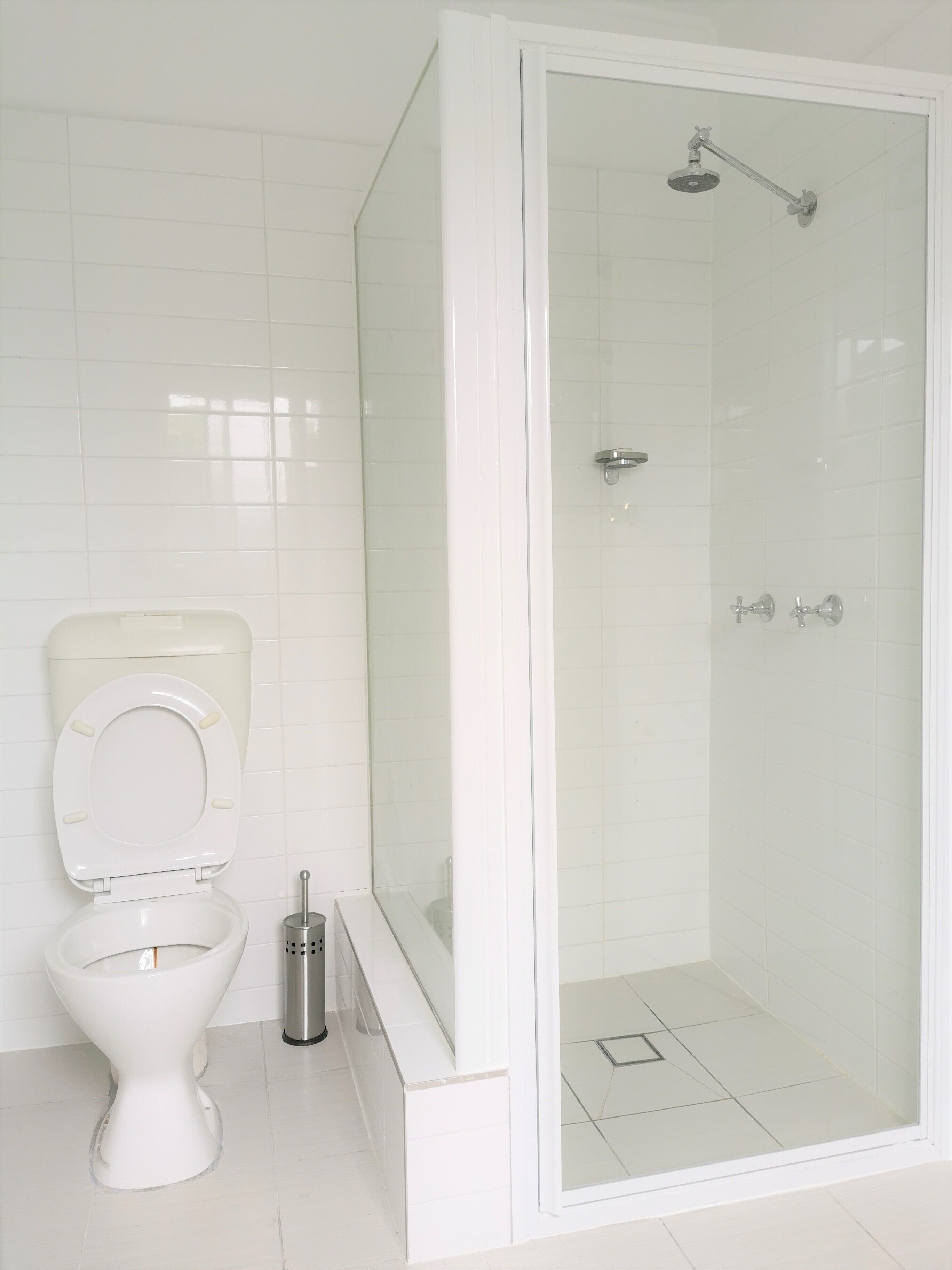 Un bagno con il water, un box doccia e uno scopino.