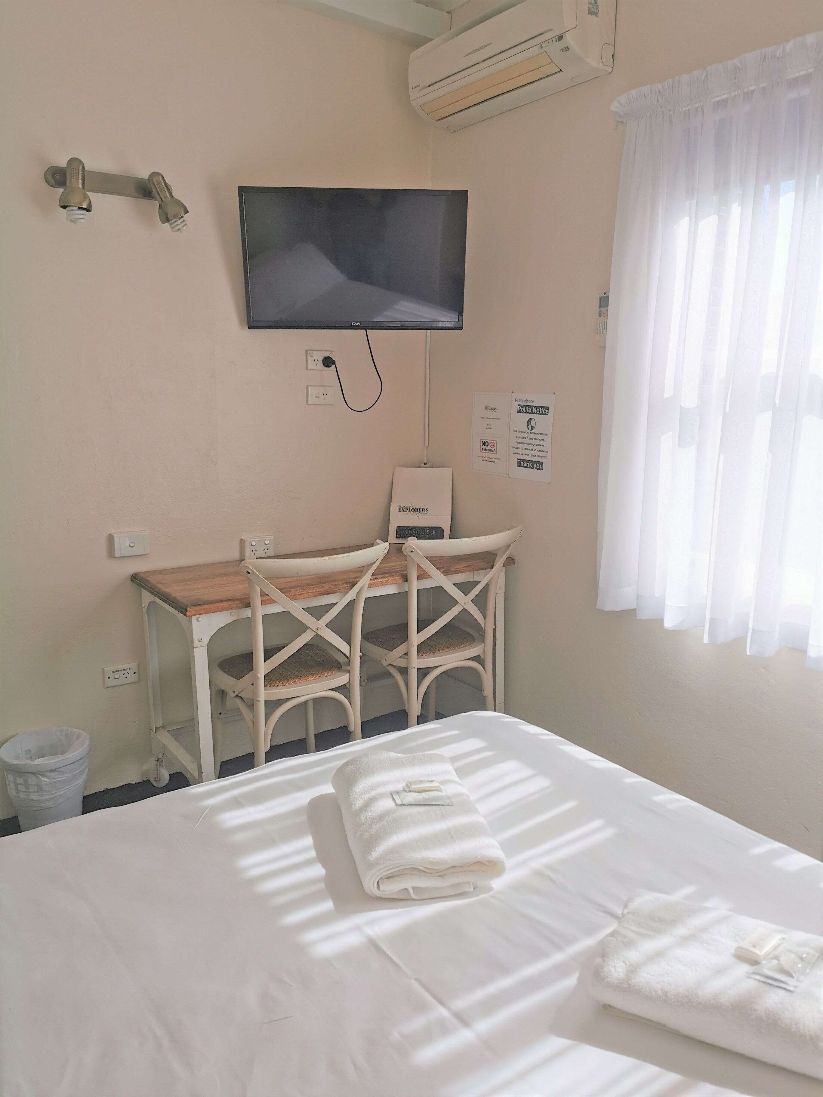 A hotel room with a bed, a desk, a chair, a TV, an air conditioner, and a window with curtains.