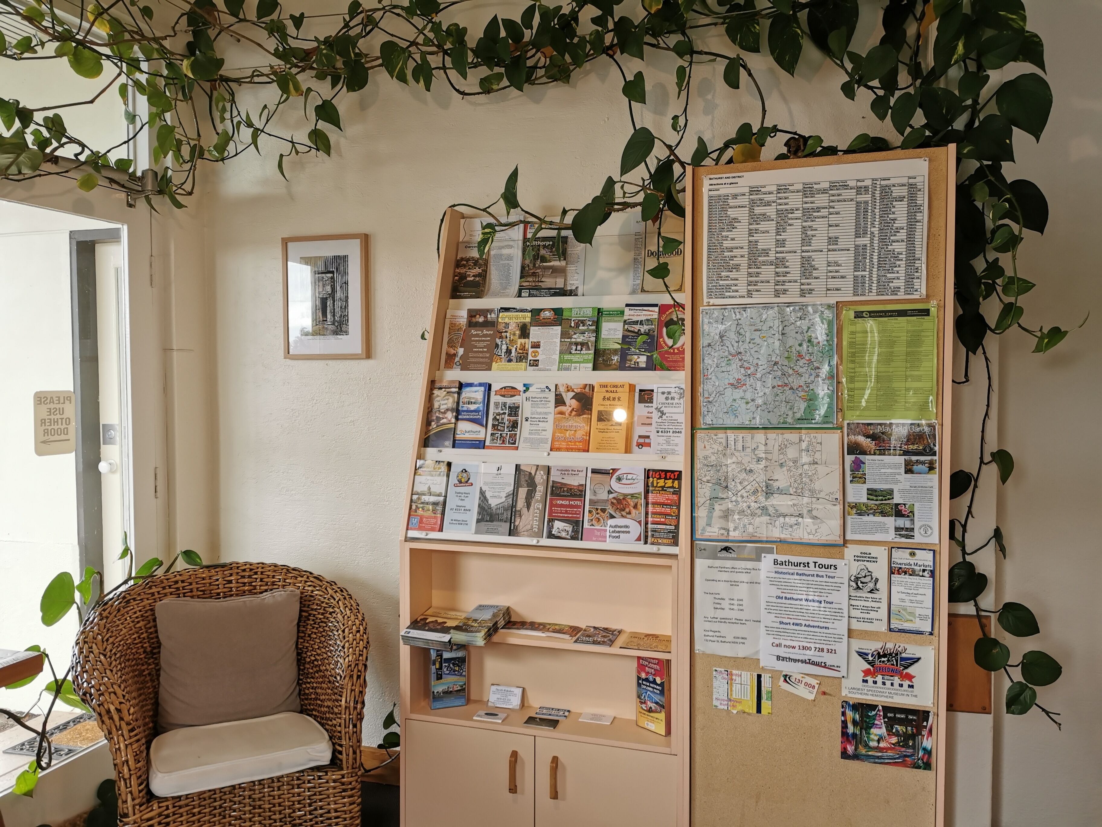 A room with a wicker chair, a bulletin board with various travel brochures, and a map.