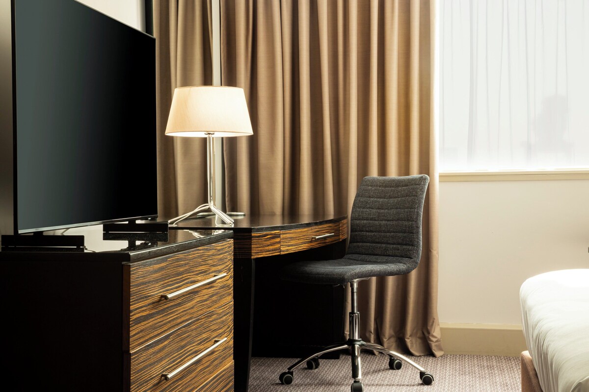 Een hotelkamer met een bureau, stoel, lamp en bed.