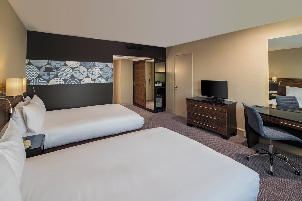 Hotelkamer met twee bedden, een bureau met stoel, een televisie en een kledingkast.
