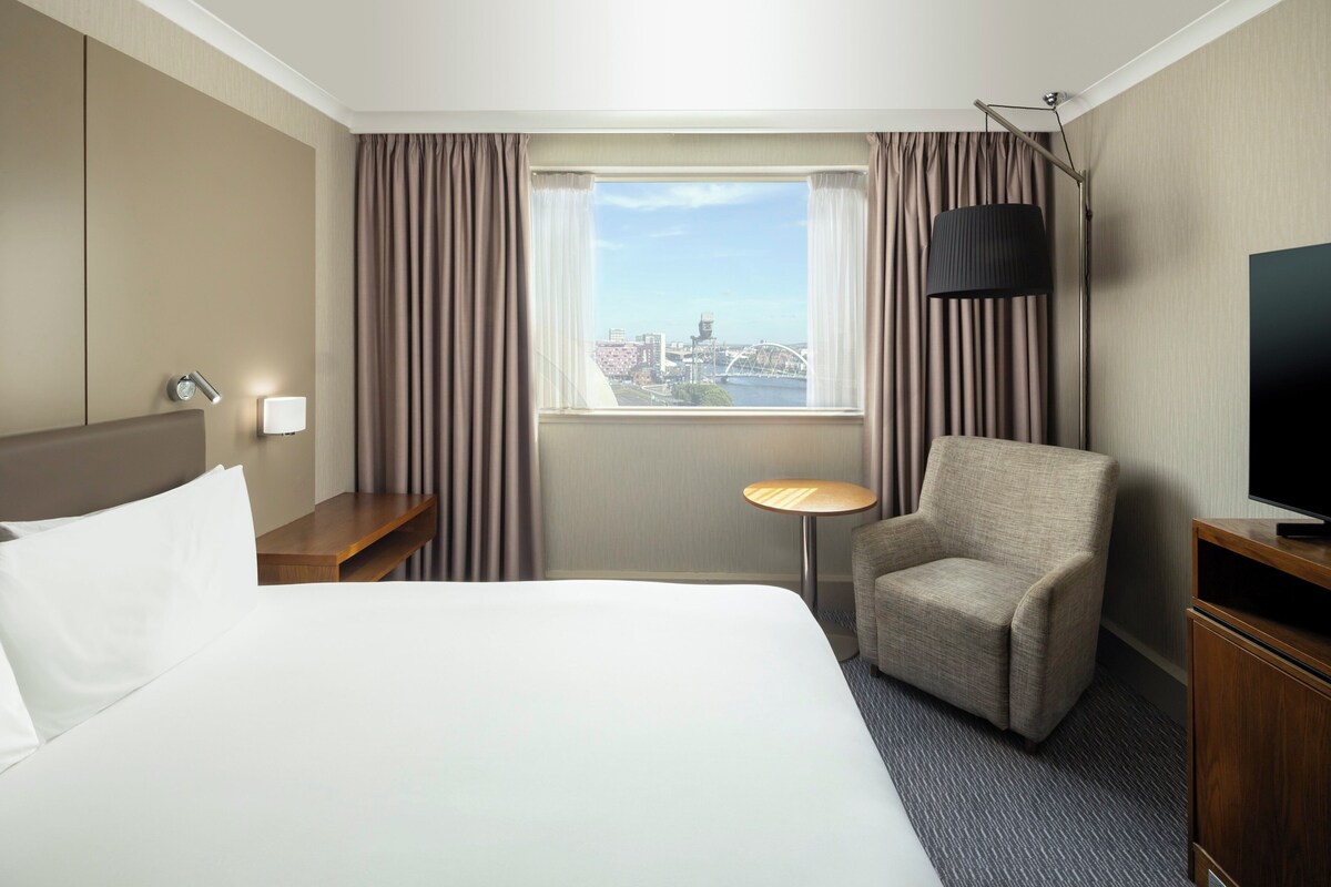 Hotelkamer met een groot bed, een stoel, een bureau, een televisie en een raam met uitzicht op de stad.