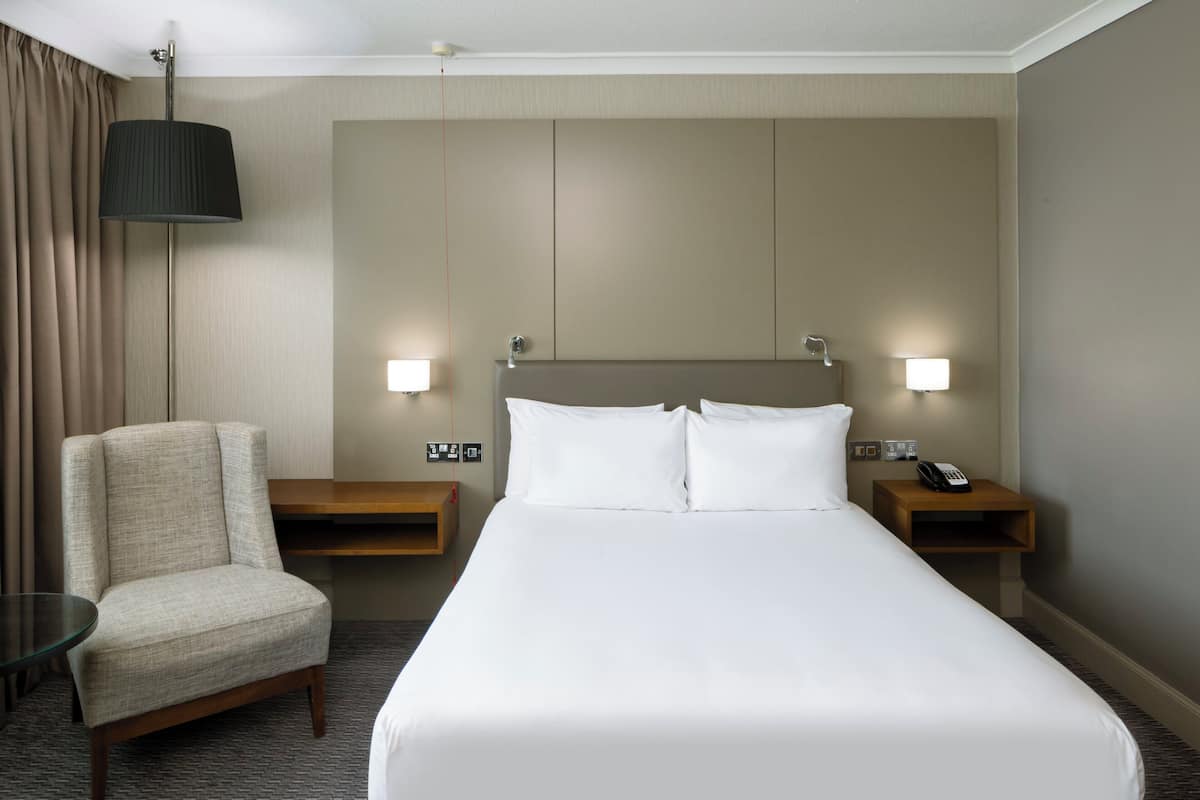 Een hotelkamer met een groot bed, twee nachtkastjes, een stoel en een lamp.