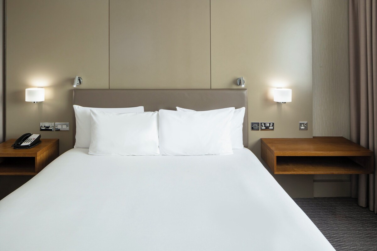 Een hotelkamer met een groot bed, twee nachtkastjes, een telefoon en wandlampen.