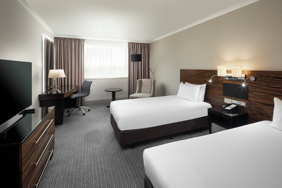 Een hotelkamer met twee bedden, een bureau met lamp, een stoel, een televisie en een nachtkastje met telefoon.