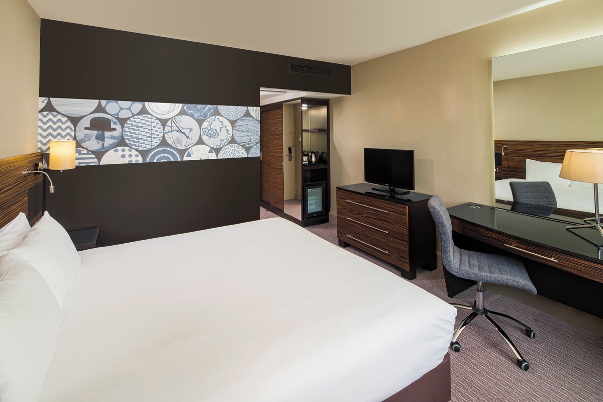 Een hotelkamer met een groot bed, een bureau met stoel, een televisie, een kast en een spiegel.