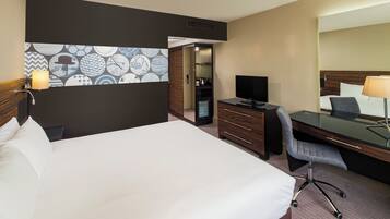 Une chambre d’hôtel avec un grand lit, un bureau avec une chaise, une télévision, une commode et un miroir.