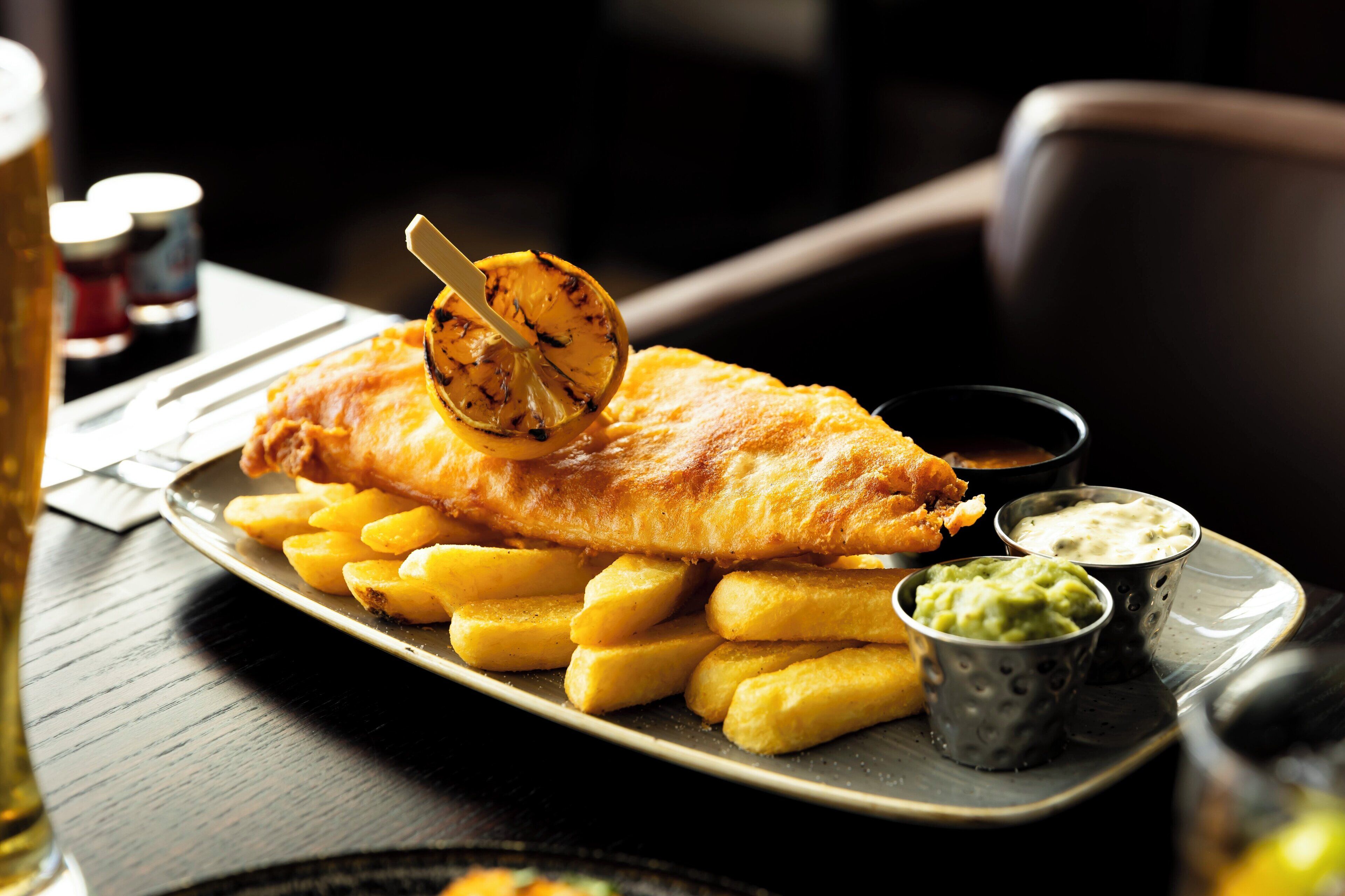 A plate of fish and chips with a lemon wedge and two dipping sauces.