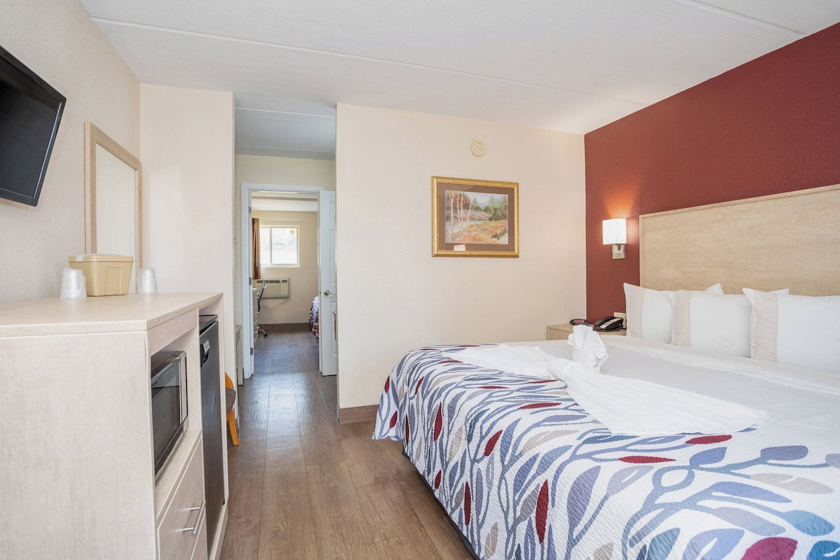 A hotel room with a bed, a desk with a mirror, a painting on the wall, and a nightstand with a lamp.