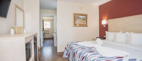 A hotel room with a bed, a desk, a television, and a painting on the wall.