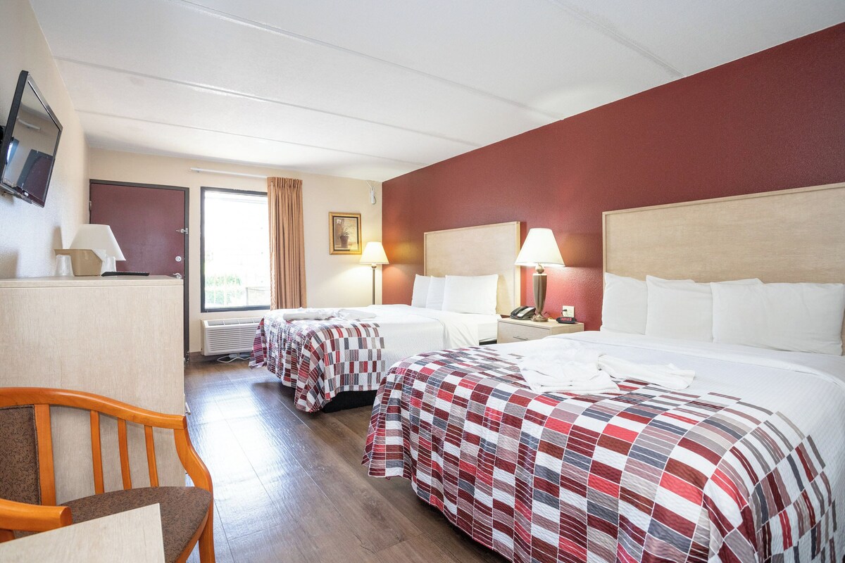 A hotel room with two beds, a desk, a chair, a TV, and a window with curtains.