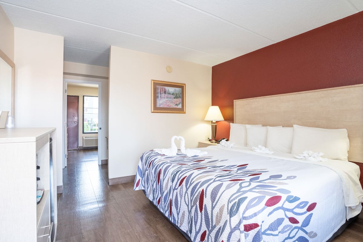 A hotel room with a bed, a desk, a lamp, and a painting on the wall.