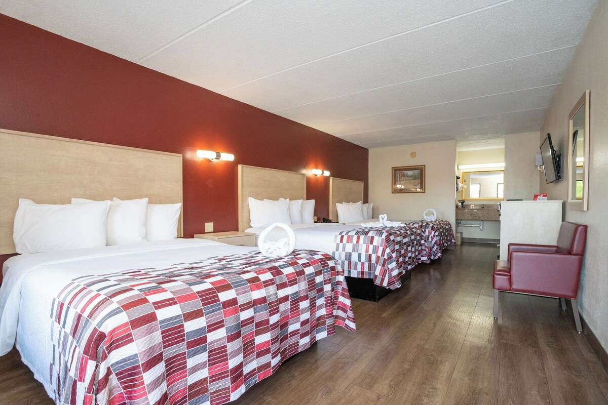 A hotel room with three beds, a red chair, and a kitchenette.
